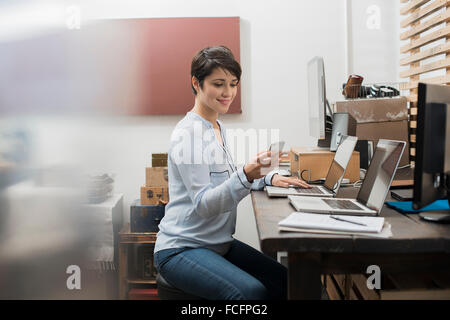 A woman in a home office with a desk with two laptops, checking her smart phone. Stock Photo
