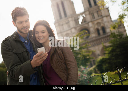 Two people, a couple standing close together taking a selfy outside the historic Notre Dame cathedral in Paris. Stock Photo