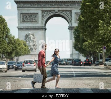 A couple hand in hand carrying shopping bags and crossing the road by a historic monument Stock Photo