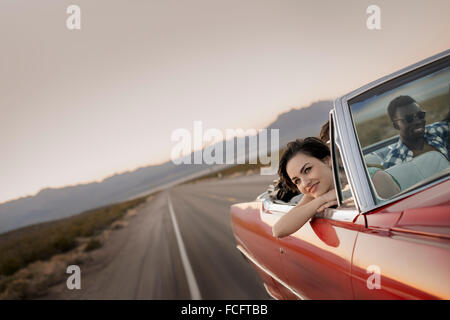A group of friends in a red open top convertable classic car on a road ...