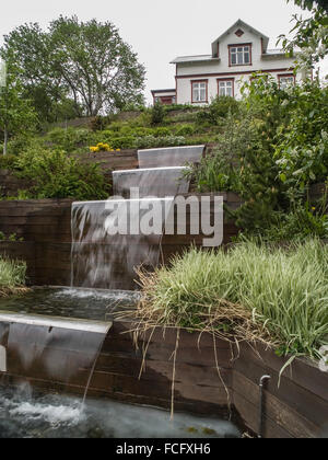 Cascading pond in landscaped garden in front of white house in Akureyri, Iceland.
