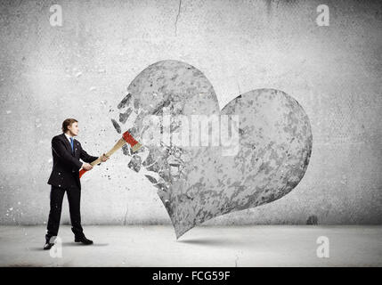 Young businessman breaking stone heart with axe Stock Photo