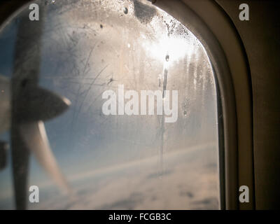 Spinning propeller grid of land, clouds and blue sky seen through aeroplane window with condensation and dripping water on it. Stock Photo