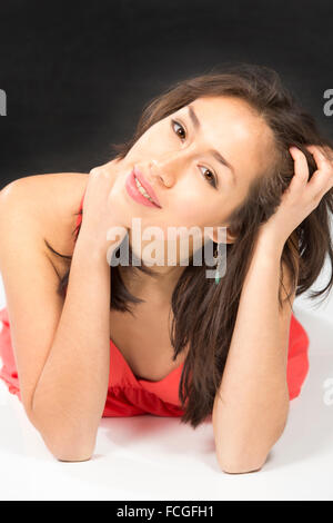 Closeup portrait of beautiful young woman smiling, lying on floor, head tilted and propped in hands, elbows down. Stock Photo