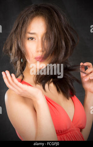 Closeup portrait of beautiful young woman with messed up hair over half of face, in tangerine dress against black background.. Stock Photo