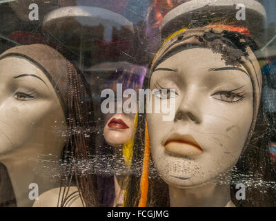Three female caucasian mannequin heads wearing scarves with very serious expressions in a scratched up store front window in Man Stock Photo