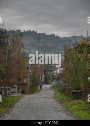 Single male walking down long road towards village in Maramures Region, Romania, Europe on a cloudy hazy day. Stock Photo