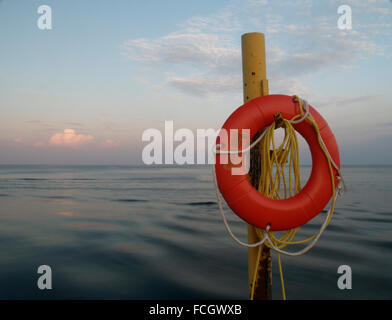 Orange round life preserver on a rusted yellow pole at sunset in front of the lake in downtown Oakville, Ontario, Canada. Stock Photo