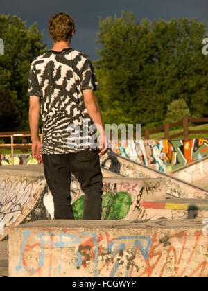Young male standing with back to camera in skateboard park covered in graffiti in Bronte, Oakville, Ontario, Canada. Stock Photo
