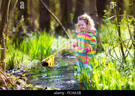 Children playing outdoors. Preschool kids catching frog with net. Boy and girl fishing in forest river. Stock Photo