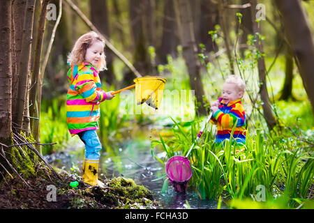 Children playing outdoors. Preschool kids catching frog with net. Boy and girl fishing in forest river. Stock Photo