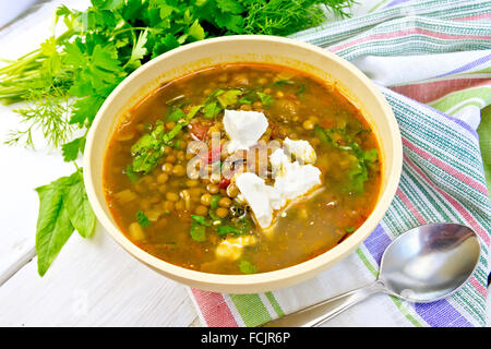 Lentil soup with spinach, tomatoes and feta cheese in a yellow bowl, spoon on a napkin, parsley and spinach Stock Photo