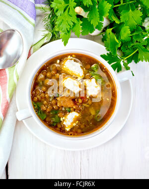 Lentil soup with spinach, tomatoes and feta cheese in a white bowl, spoon on a kitchen towel, parsley on the background light wo Stock Photo