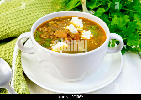 Lentil soup with spinach, tomatoes and feta cheese in a white bowl, spoon on a kitchen towel, parsley on the background board Stock Photo