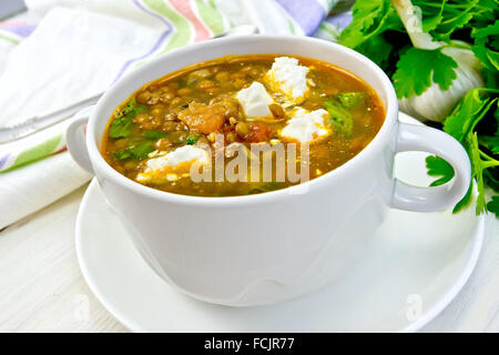 Lentil soup with spinach, tomatoes and feta cheese in a white bowl, napkin, parsley on the background light wooden boards Stock Photo