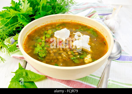 Lentil soup with spinach, tomatoes and feta cheese in a yellow bowl, spoon on a kitchen towel, parsley and spinach Stock Photo