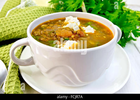 Lentil soup with spinach, tomatoes and feta cheese in a white bowl, spoon on a green napkin, parsley on the background wood Stock Photo