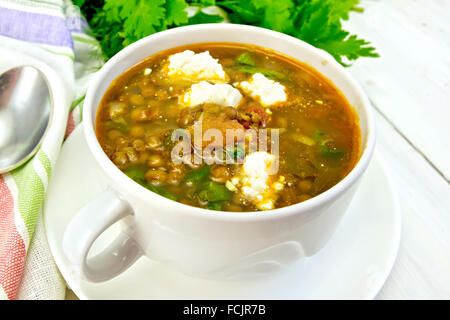 Lentil soup with spinach, tomatoes and feta cheese, napkin, spoon, parsley on a light wooden board Stock Photo