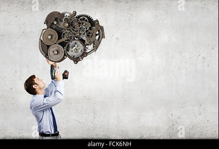 Young businessman using drill to fix gear mechanism Stock Photo