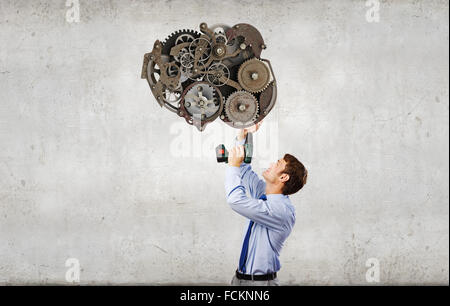 Young businessman using drill to fix gear mechanism Stock Photo