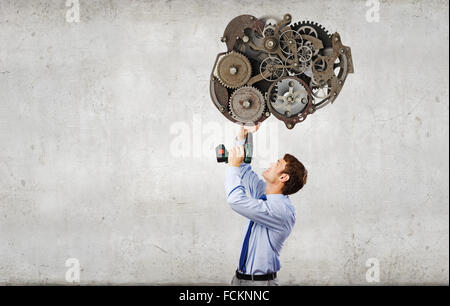 Young businessman using drill to fix gear mechanism Stock Photo