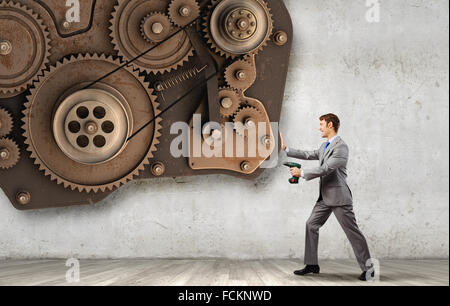 Young businessman using drill to fix gear mechanism Stock Photo