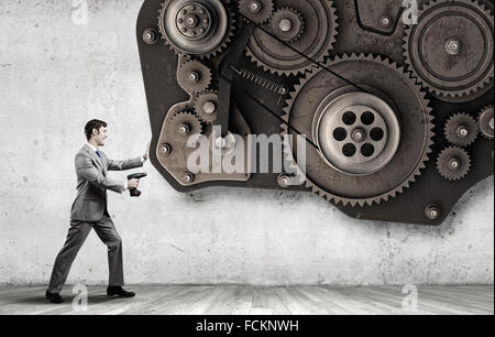 Young businessman using drill to fix gear mechanism Stock Photo