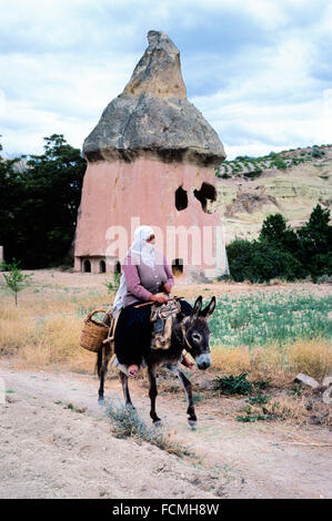 Turkish Peasant Woman Riding a Donkey in Front of a Volcanic Fairy Chimney or Volcanic Hoodoo Converted into a Troglodyte House with Rock-Cut Windows in the Soft Tufa Rock Cappadocia Turkey Stock Photo