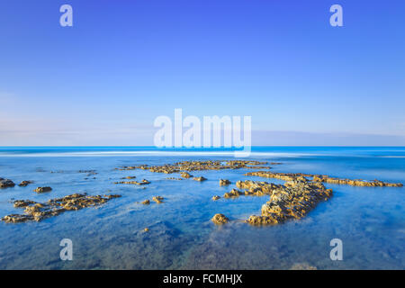Rocks in a blue ocean under a clear sky on sunrise at morning. Tuscany, Italy. Long exposure photography Stock Photo