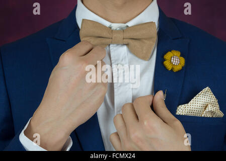 Man in blue suit with coffee cream bowtie color, flower brooch, and dot pattern handkerchief, close up, adjusting bowtie Stock Photo