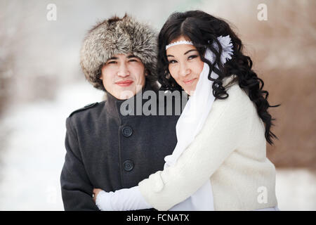 Beautiful wedding couple, asian bride and groom embraced. Young man in winter coat, fur hat, lady wearing dress with sheepskin, veil. Cold season warm clothing. Close-up portrait. Stock Photo