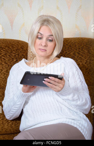 Blonde sitting on the couch with tablet computer Stock Photo