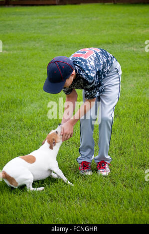 Young baseball player outside playing with his white jack russell dog. Stock Photo