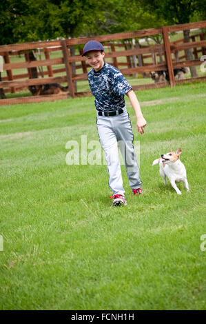 Youth baseball player playing with his dog in the yard outdoors. Stock Photo