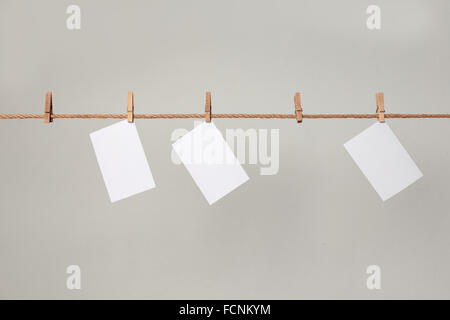 white photo paper. Hanging on a clothesline with clothespins. On a gray background Stock Photo