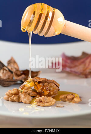 honey spilling from a wooden spoon on walnut Stock Photo