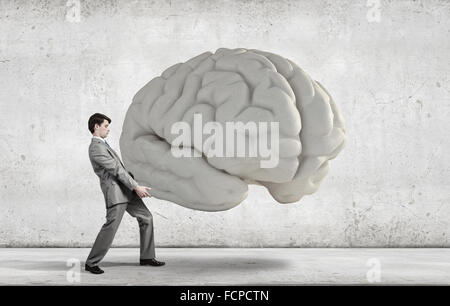 Businessman making effort to carry huge human brain Stock Photo