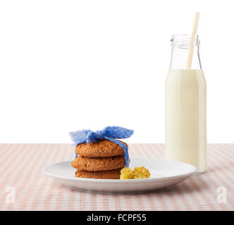 Stack of three homemade oatmeal cookies tied with blue ribbon  and yellow flowers on white plate and bottle of milk Stock Photo