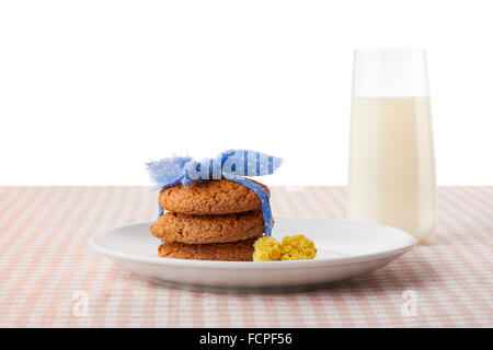 Stack of three homemade oatmeal cookies tied with blue ribbon and yellow flowers on white plate and glass of milk Stock Photo