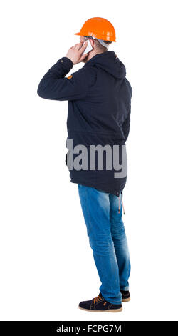Backview of an engineer in construction helmet stands and using a mobile phone. Standing young guy. Rear view people collection. backside view of person. Isolated over white background. Engineer is a businesswoman talking on the phone. Stock Photo