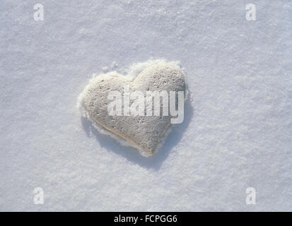 White stone heart resting on frozen crust of pristine snow. Stock Photo