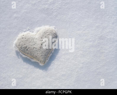 White stone heart resting on frozen crust of pristine snow. Stock Photo