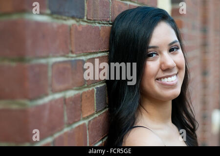 Beautiful and happy teen girl leaning on a brick wall building. Stock Photo