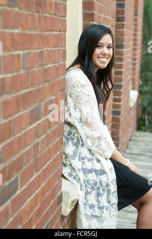 Beautiful and happy teen girl sitting in a window of a brick wall building. Stock Photo