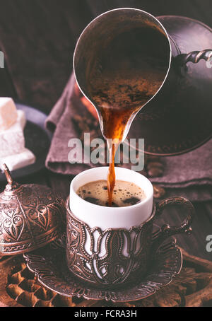Pouring turkish coffee into traditional embossed metal cup.Toned Stock Photo