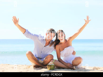 Cheerful couple sitting on beach and waving hands Stock Photo