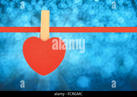 Valentine day template, one red wooden heart with clothes pin on textile ribbon over winter snow blue glitter blur