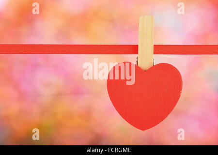 Valentine day template, one red wooden heart with clothes pin on textile ribbon over bright colorful glitter blur