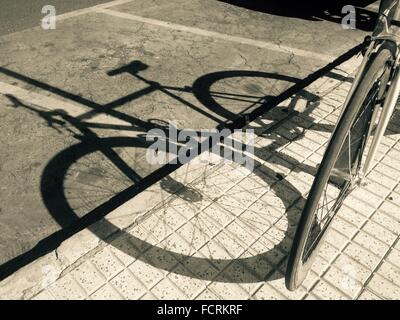 Shadow of parked bicycle over the asphalt road. Black and white shot Stock Photo