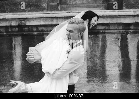 groom carries bride in his arms Stock Photo